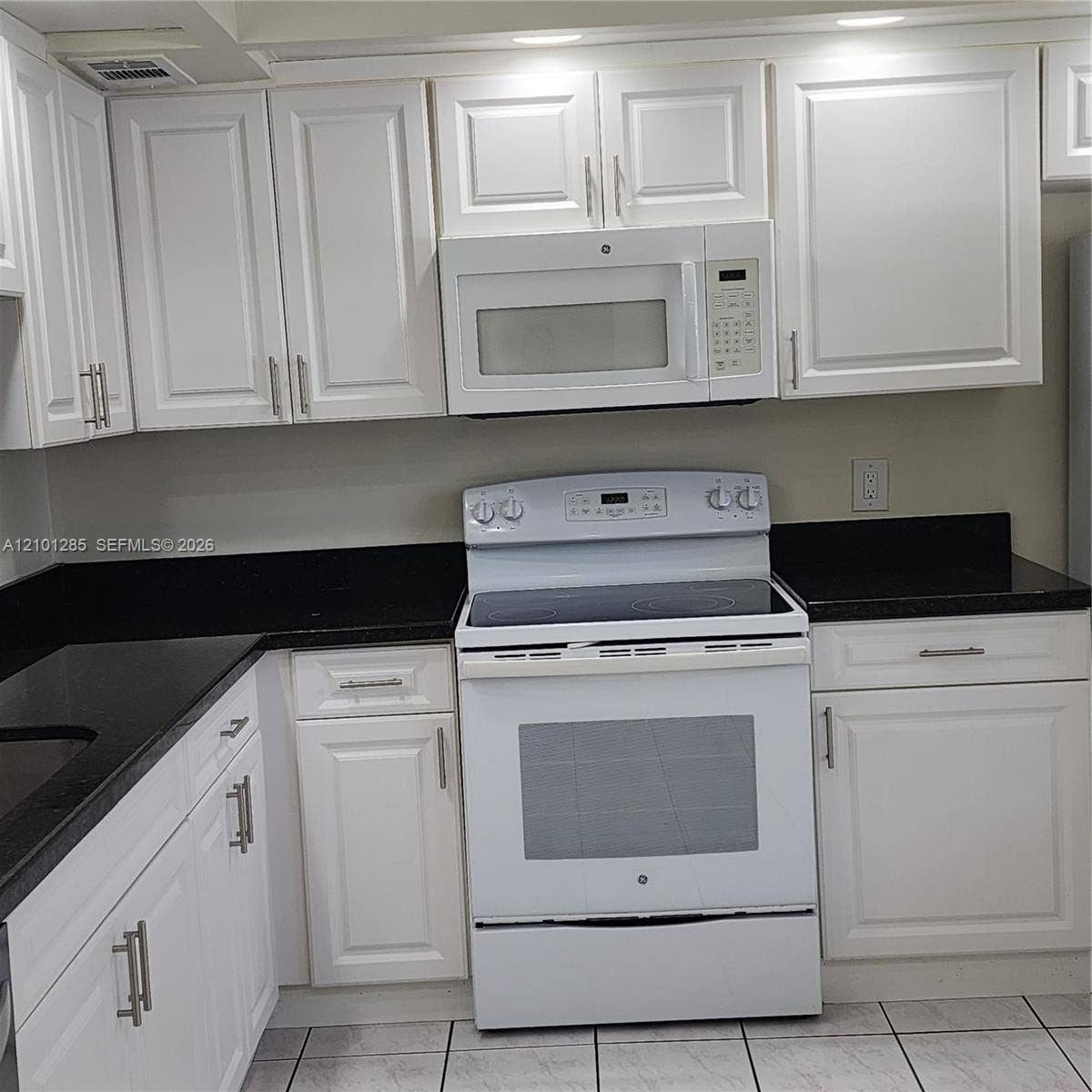 Kitchen featuring white shaker-style cabinetry, dark stone-finish countertops, and white appliances including an electric range and built-in microwave