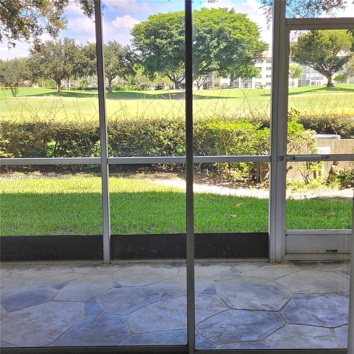 Screened-in patio with flagstone-patterned flooring and direct access to an outdoor area with mature landscaping