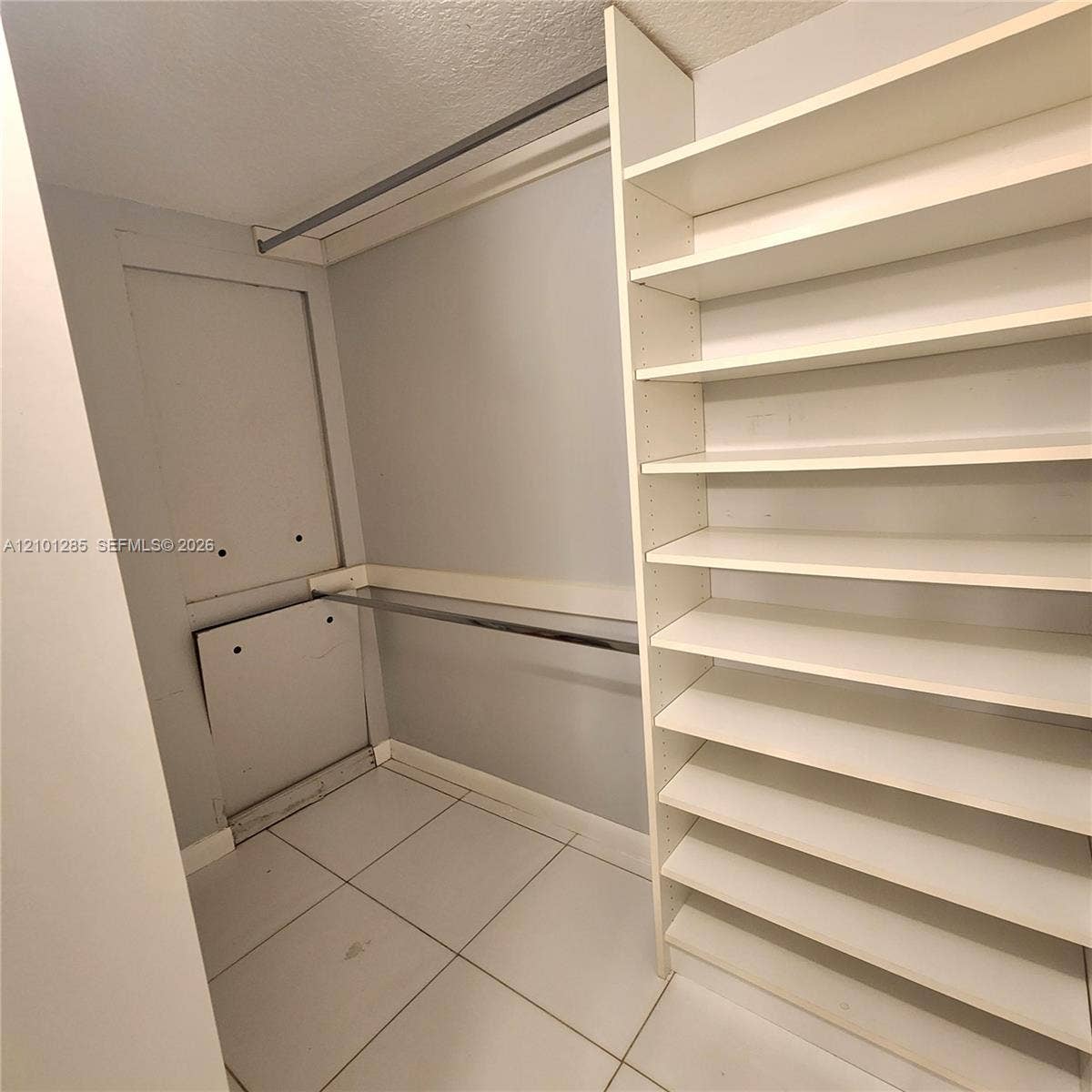 Walk-in storage space featuring ceramic tile flooring, built-in shelving, and dual metal clothing rods