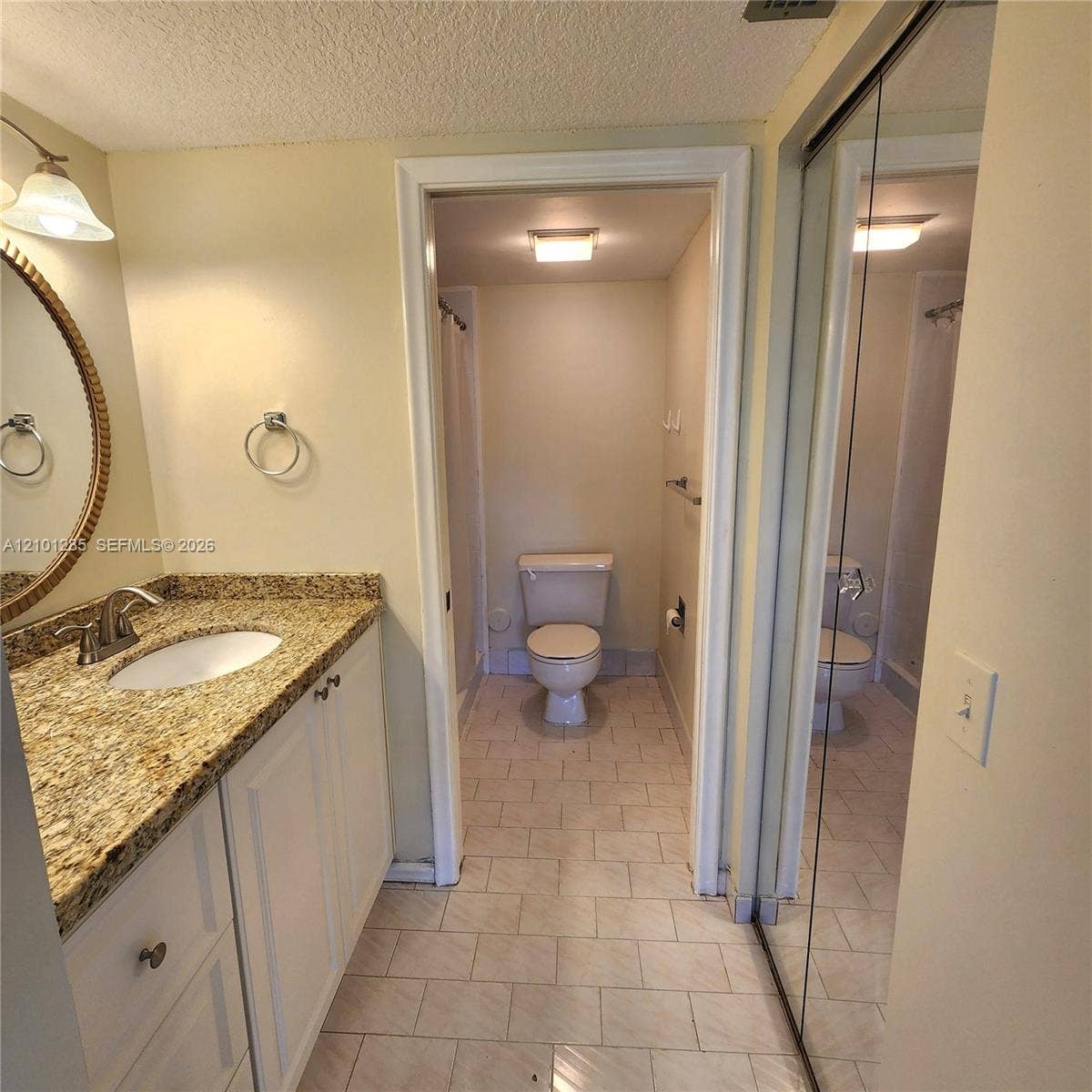 Bathroom featuring a stone-look countertop, integrated oval sink, white cabinetry, circular mirror with decorative frame, and mirrored sliding closet doors