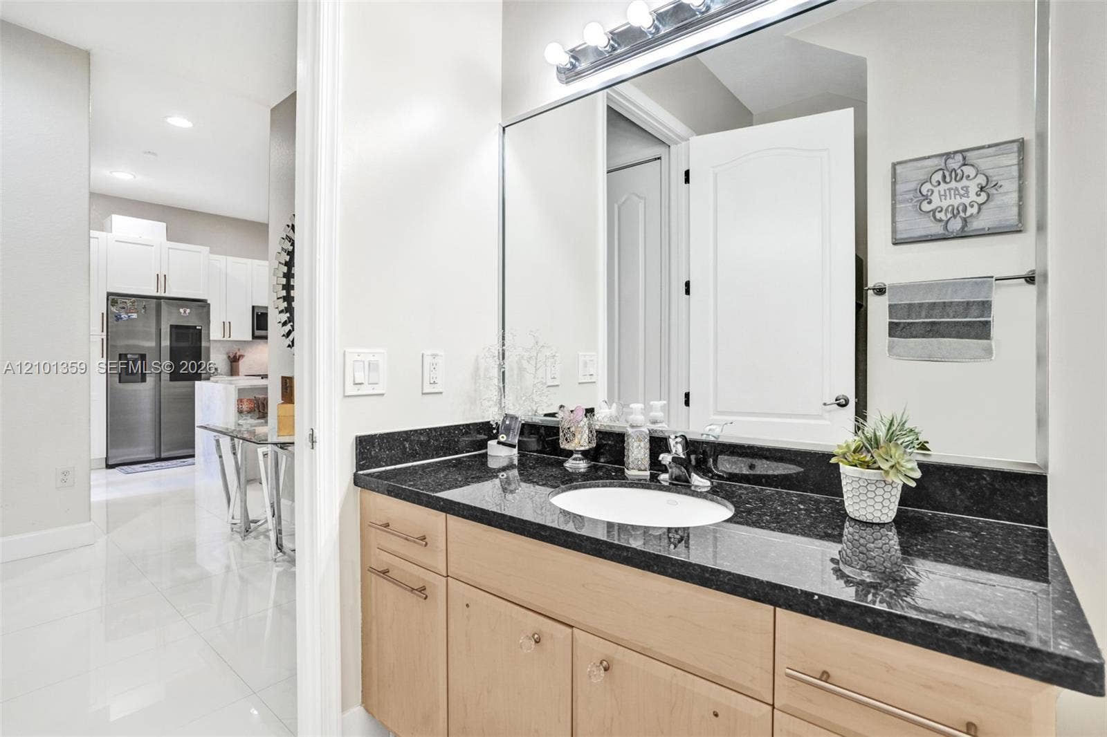 859 SW 147th Terrace, #0, Pembroke Pines, FL 33027 Bathroom vanity featuring dark stone countertops, an integrated undermount sink, light wood-finish cabinetry, a large wall-mounted mirror, and a multi-bulb light fixture