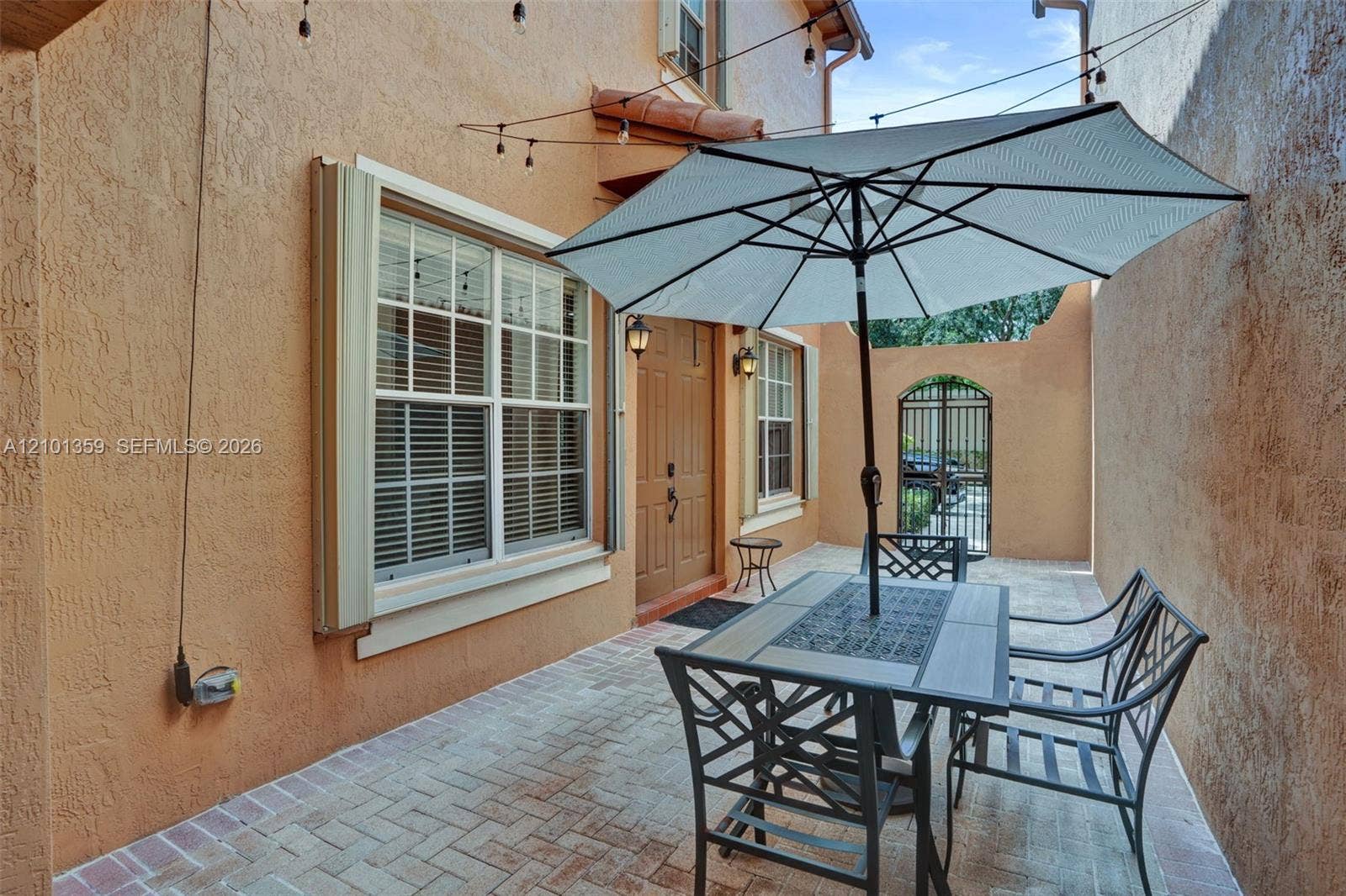859 SW 147th Terrace, #0, Pembroke Pines, FL 33027 Enclosed courtyard featuring paver flooring, stucco exterior walls, a decorative metal gate, and exterior wall-mounted lanterns