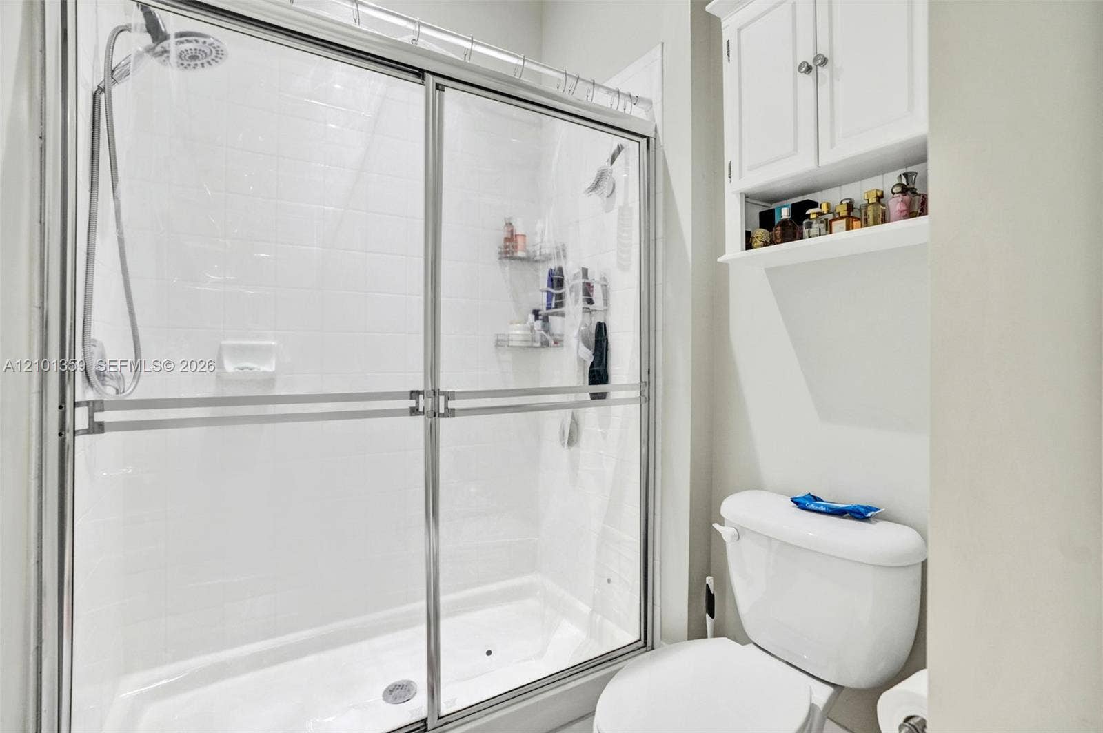 859 SW 147th Terrace, #0, Pembroke Pines, FL 33027 Walk-in shower with sliding glass doors, white subway-style tile surround, adjustable handheld shower head, and white built-in wall cabinetry