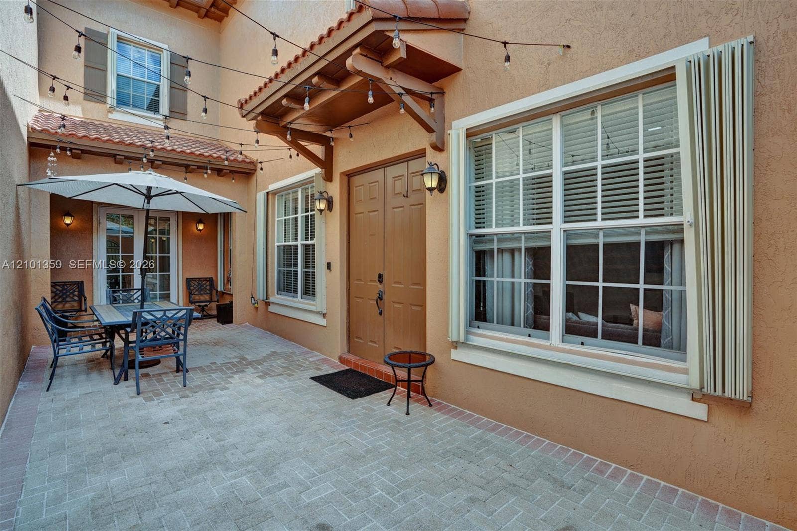 859 SW 147th Terrace, #0, Pembroke Pines, FL 33027 Enclosed courtyard featuring a paved brick patio, double entry doors, wood-accented awning, and exterior wall-mounted light fixtures