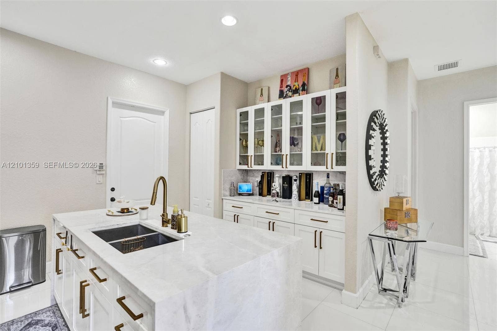 859 SW 147th Terrace, #0, Pembroke Pines, FL 33027 Kitchen island featuring stone countertops and an integrated dual-basin undermount sink with a high-arch faucet, paired with white built-in cabinetry and glass-front upper displays
