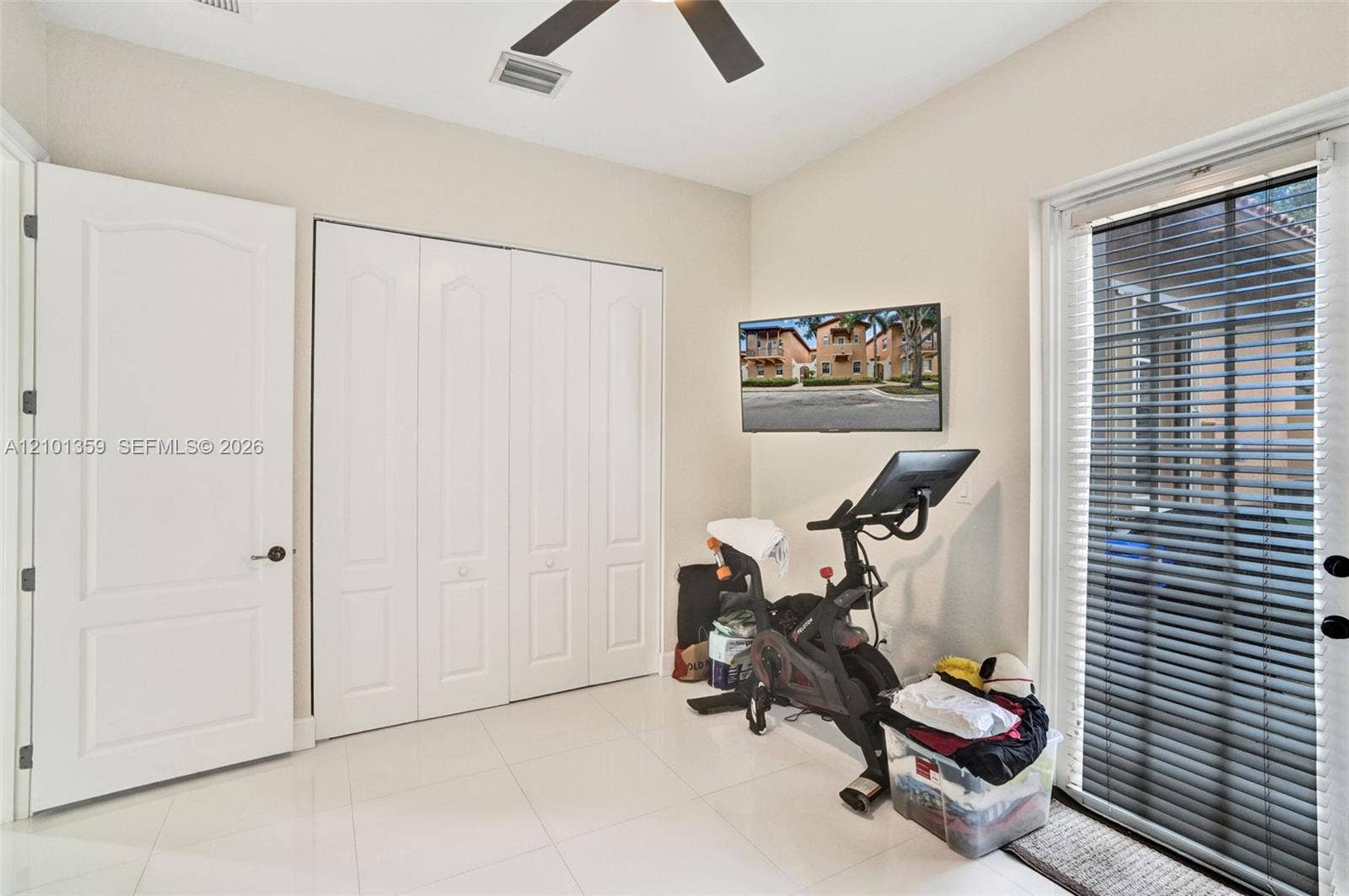 859 SW 147th Terrace, #0, Pembroke Pines, FL 33027 Neutral-toned room featuring large-format tile flooring, four-panel folding closet doors, a ceiling fan with integrated lighting, and a glass-paned door with horizontal blinds