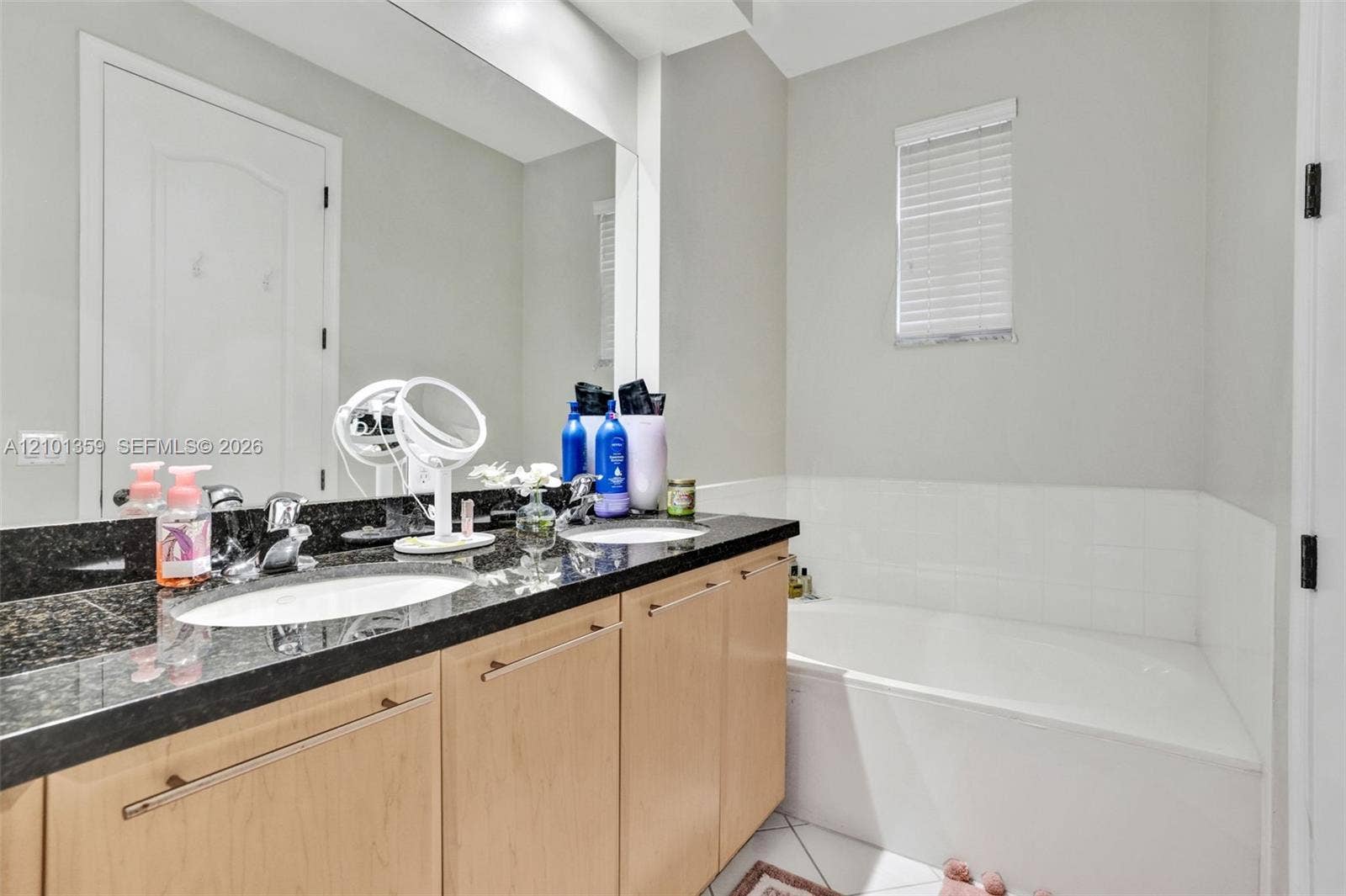 859 SW 147th Terrace, #0, Pembroke Pines, FL 33027 Dual-sink vanity with dark stone countertop, light-wood cabinetry, large wall-mounted mirror, and tile-surround bathtub
