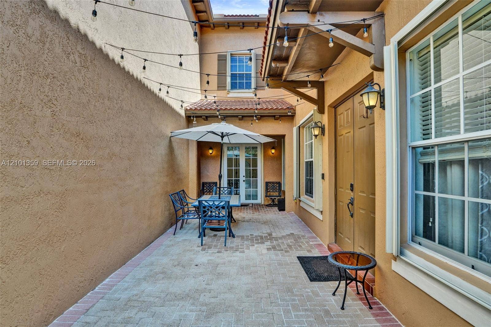 859 SW 147th Terrace, #0, Pembroke Pines, FL 33027 Enclosed courtyard featuring herringbone-patterned paver flooring, stucco wall finish, terracotta-style roof accents, and double-door entry with exterior sconce lighting