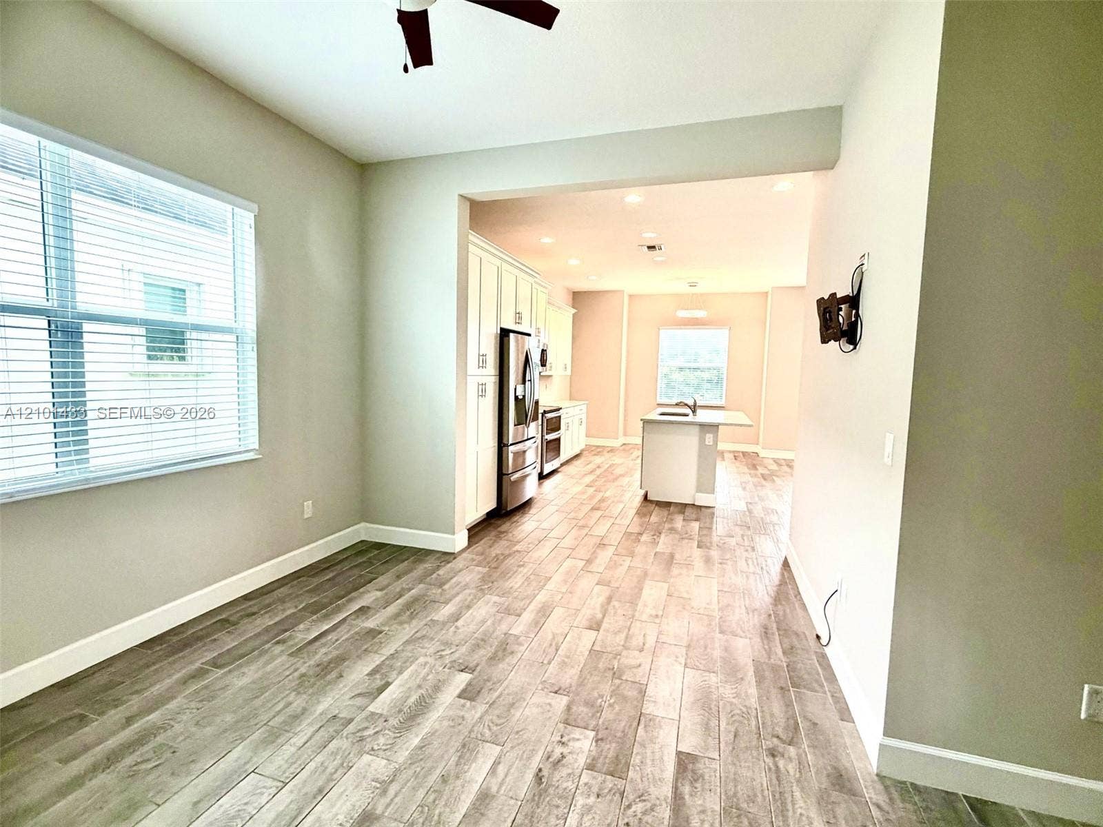 Open-concept living space with wood-finish flooring, a ceiling fan, and a large window with horizontal blinds