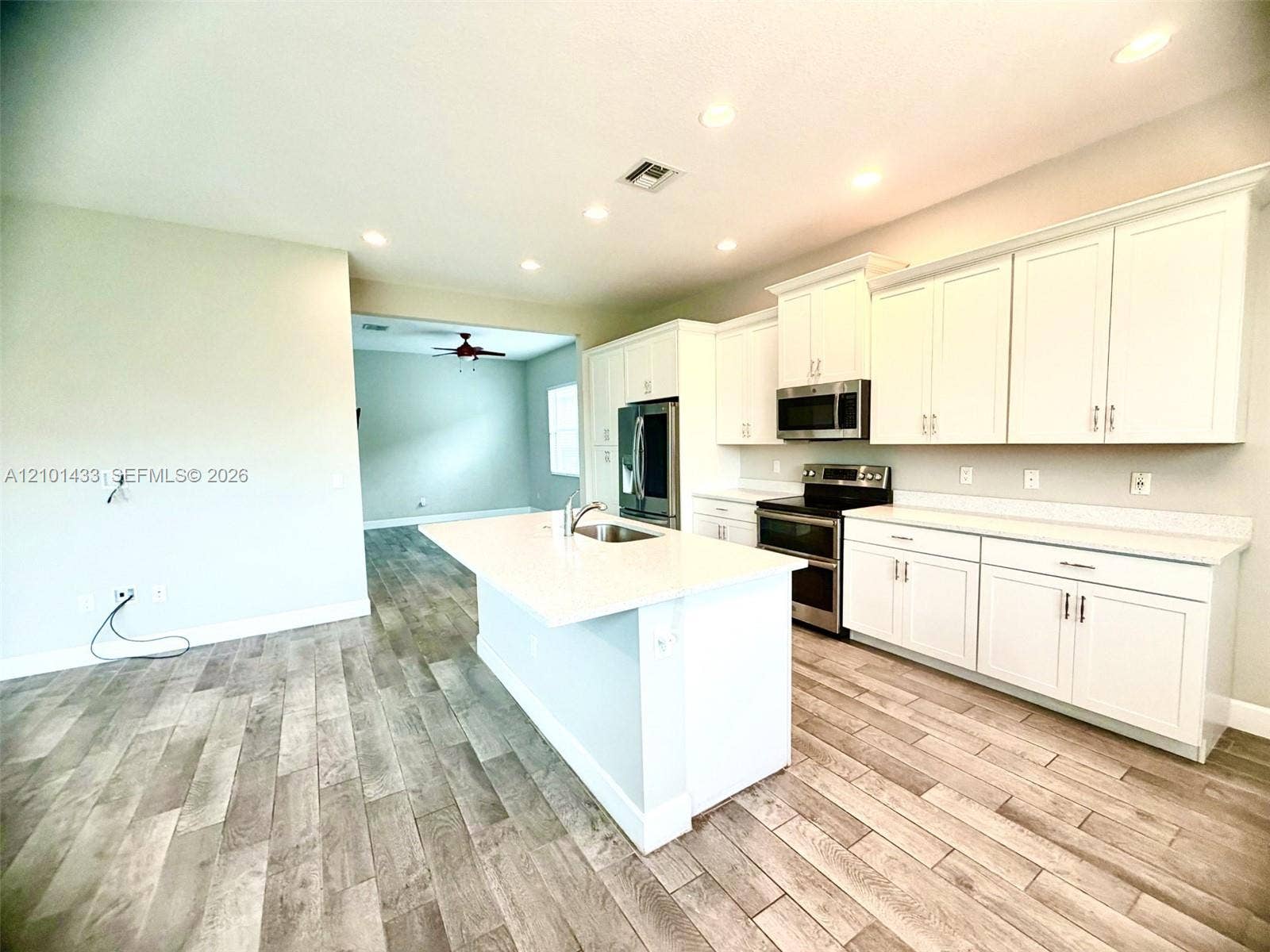 White kitchen cabinetry with stainless steel appliances, a kitchen island featuring a stainless steel sink, and wood-finish flooring