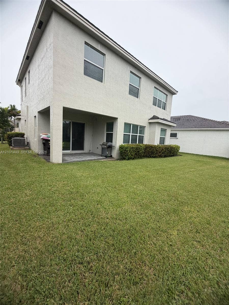Two-story exterior with stucco finish, covered patio, and ground-level windows, surrounded by a landscaped lawn