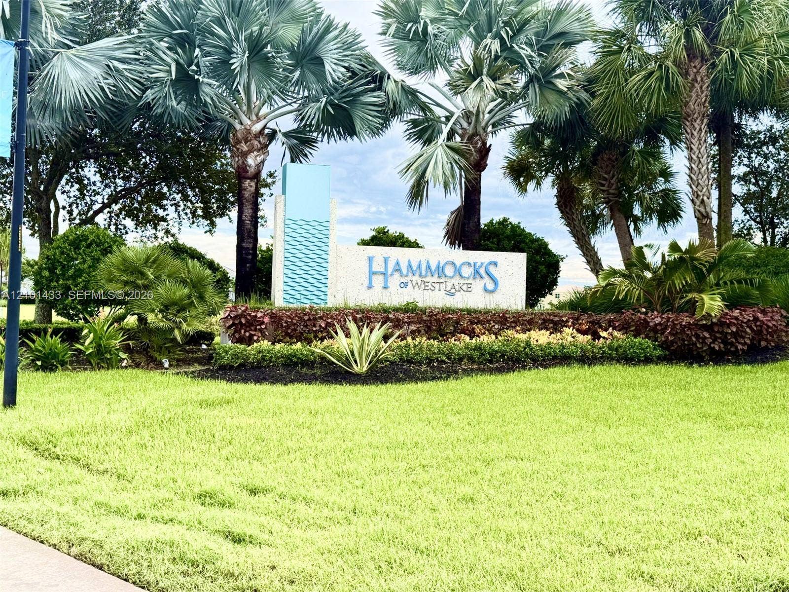 Entry monument with integrated signage, surrounded by mature palm trees and diverse landscaping, set against a manicured lawn