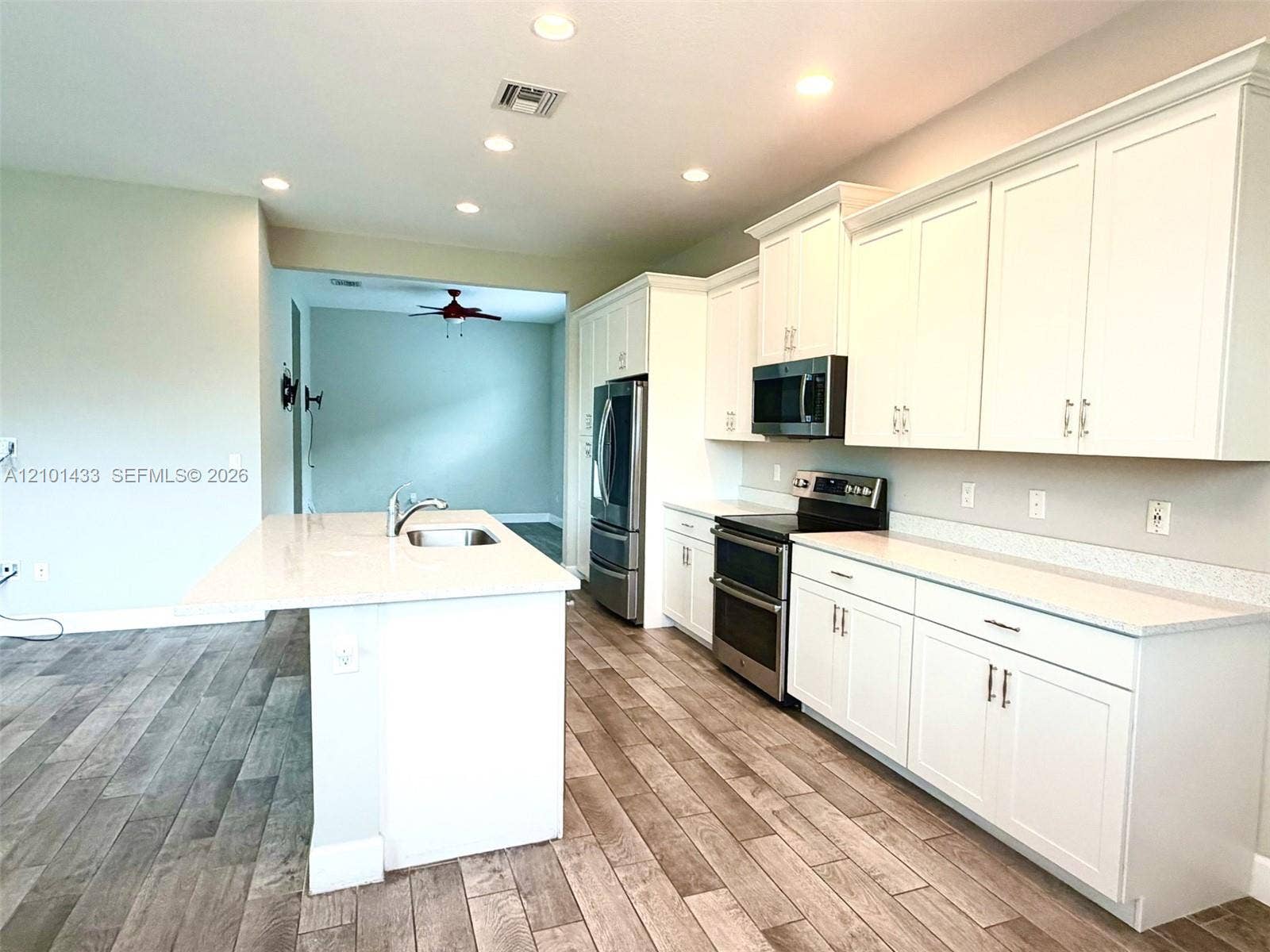 Spacious kitchen featuring wood-finish flooring, white cabinetry, integrated stainless steel appliances, and a kitchen island with an undermount sink