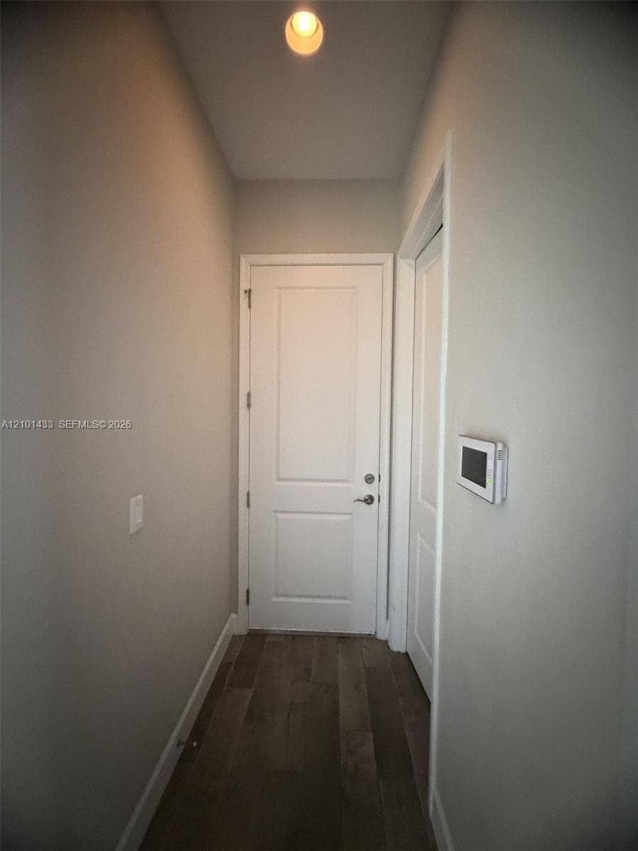Wood-finish flooring with a ceiling-mounted light fixture, white interior doors, and a wall-mounted control panel