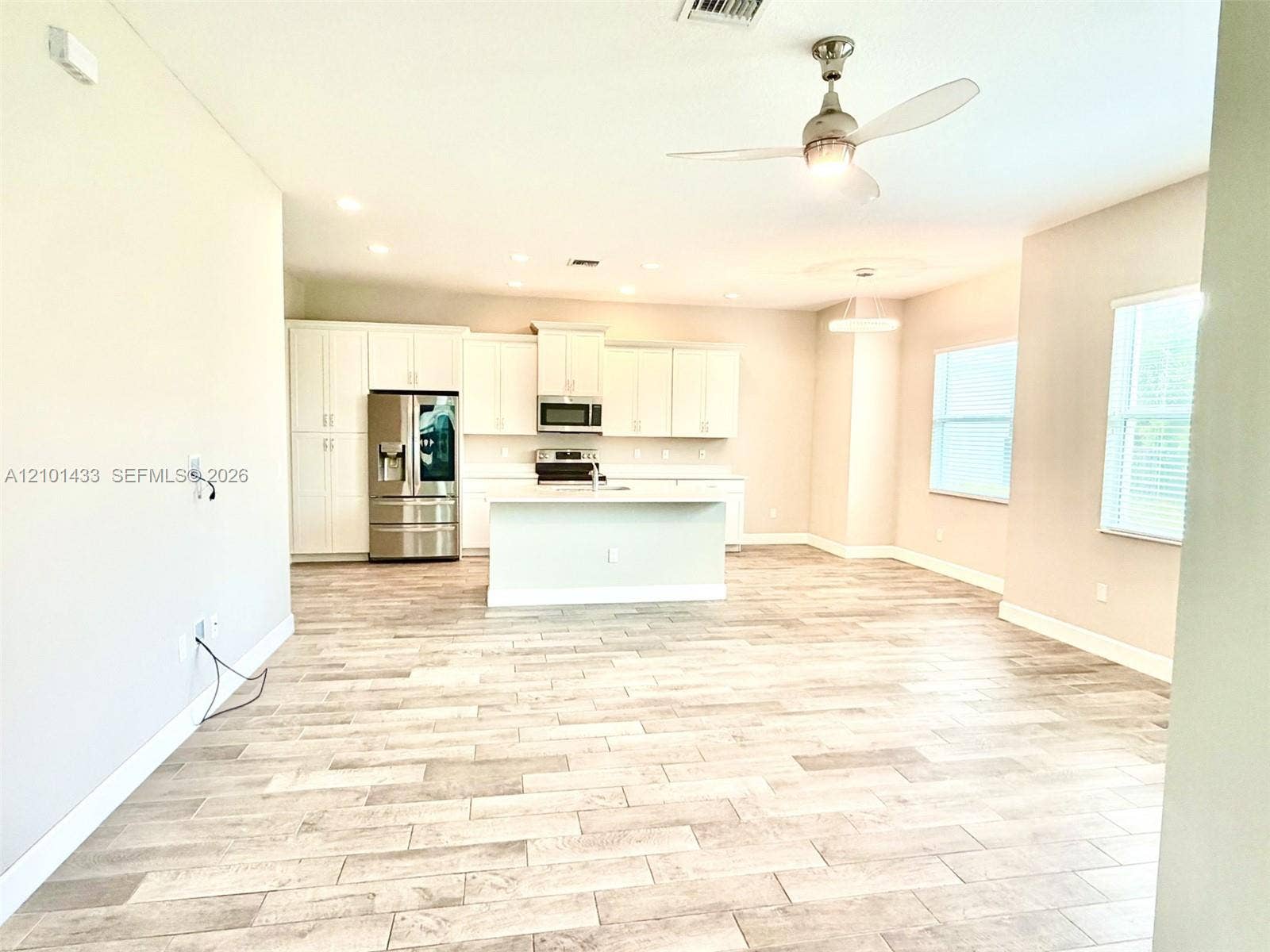 Open-concept living area with wood-finish flooring, white cabinetry, stainless steel appliances, and a ceiling fan with integrated lighting