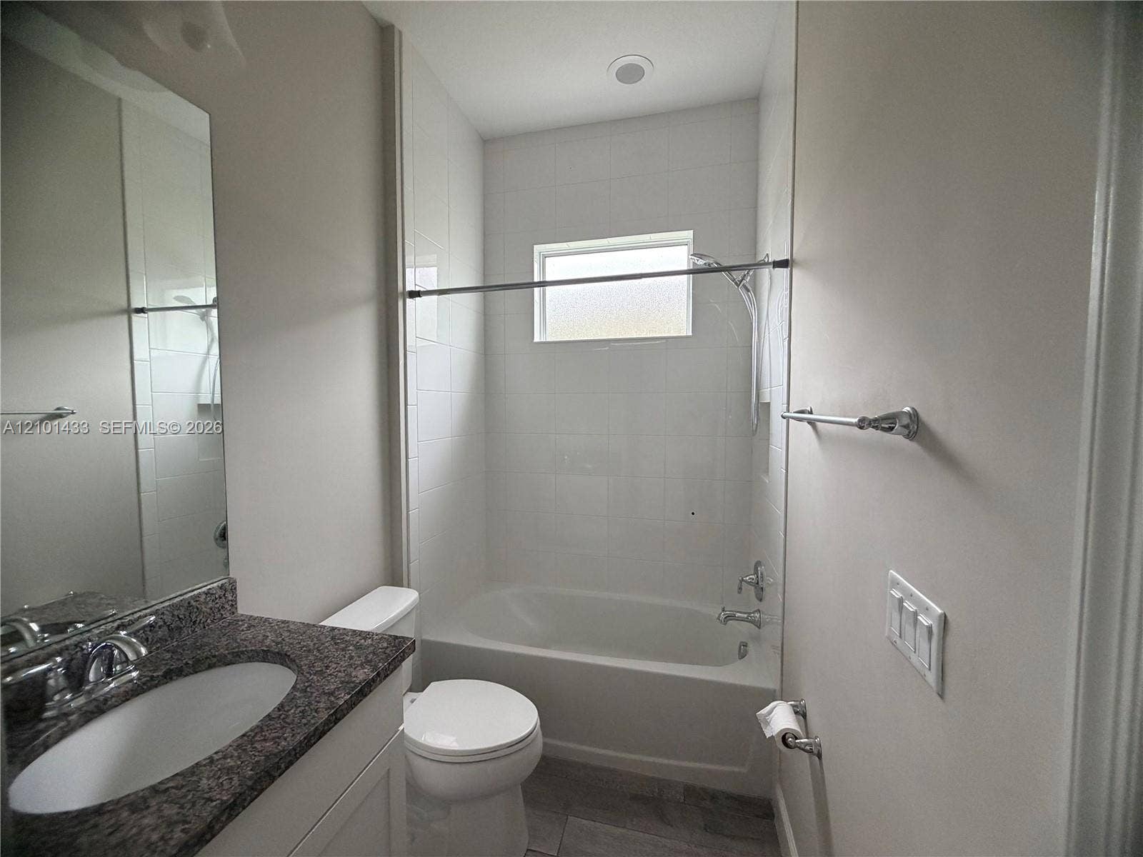 White tiled shower and tub with a privacy window, complemented by a vanity with a dark speckled countertop and an undermount sink