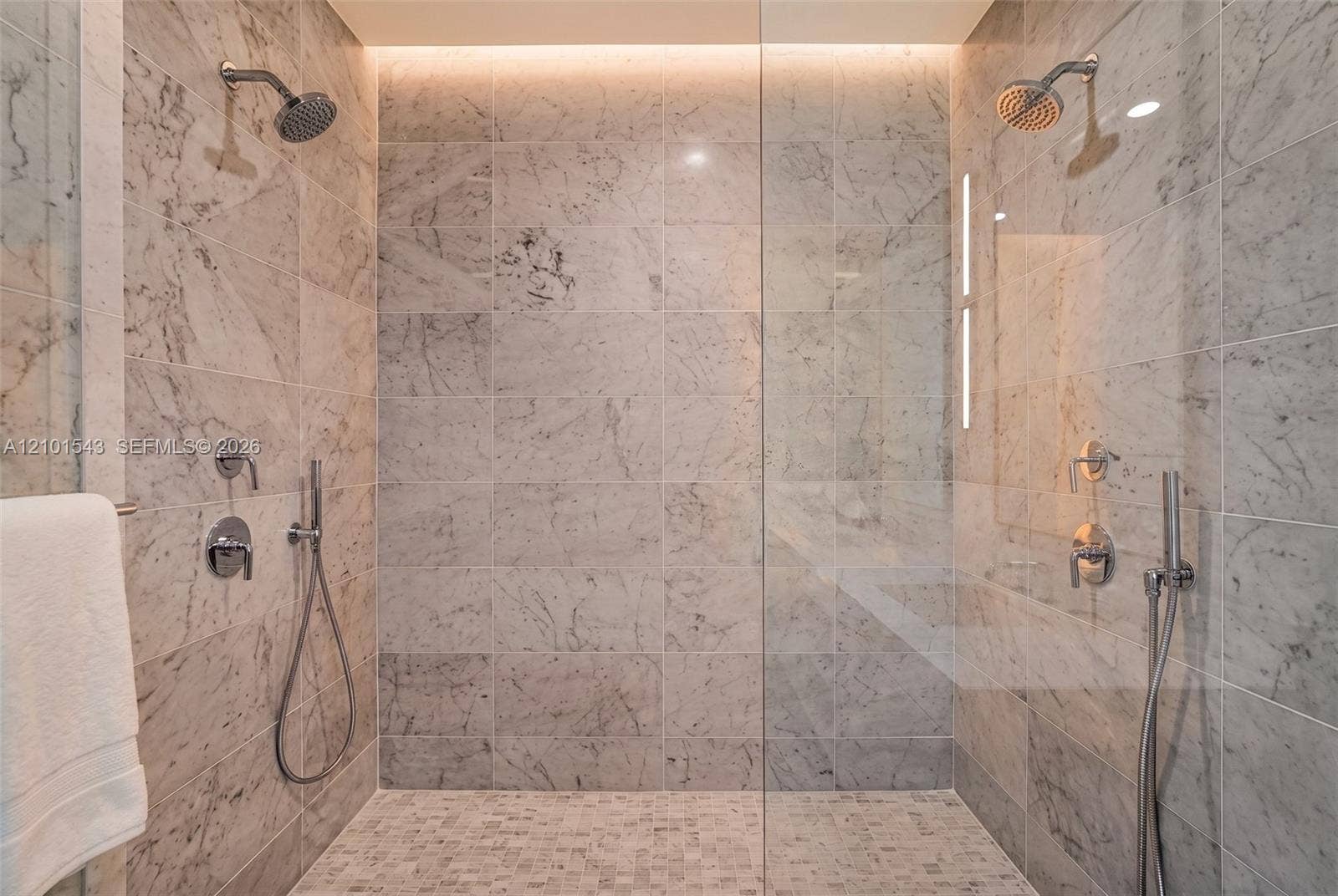 Walk-in shower featuring large-format stone wall tiling, mosaic stone flooring, dual shower heads with handheld sprayers, a frameless glass enclosure, and recessed overhead accent lighting
