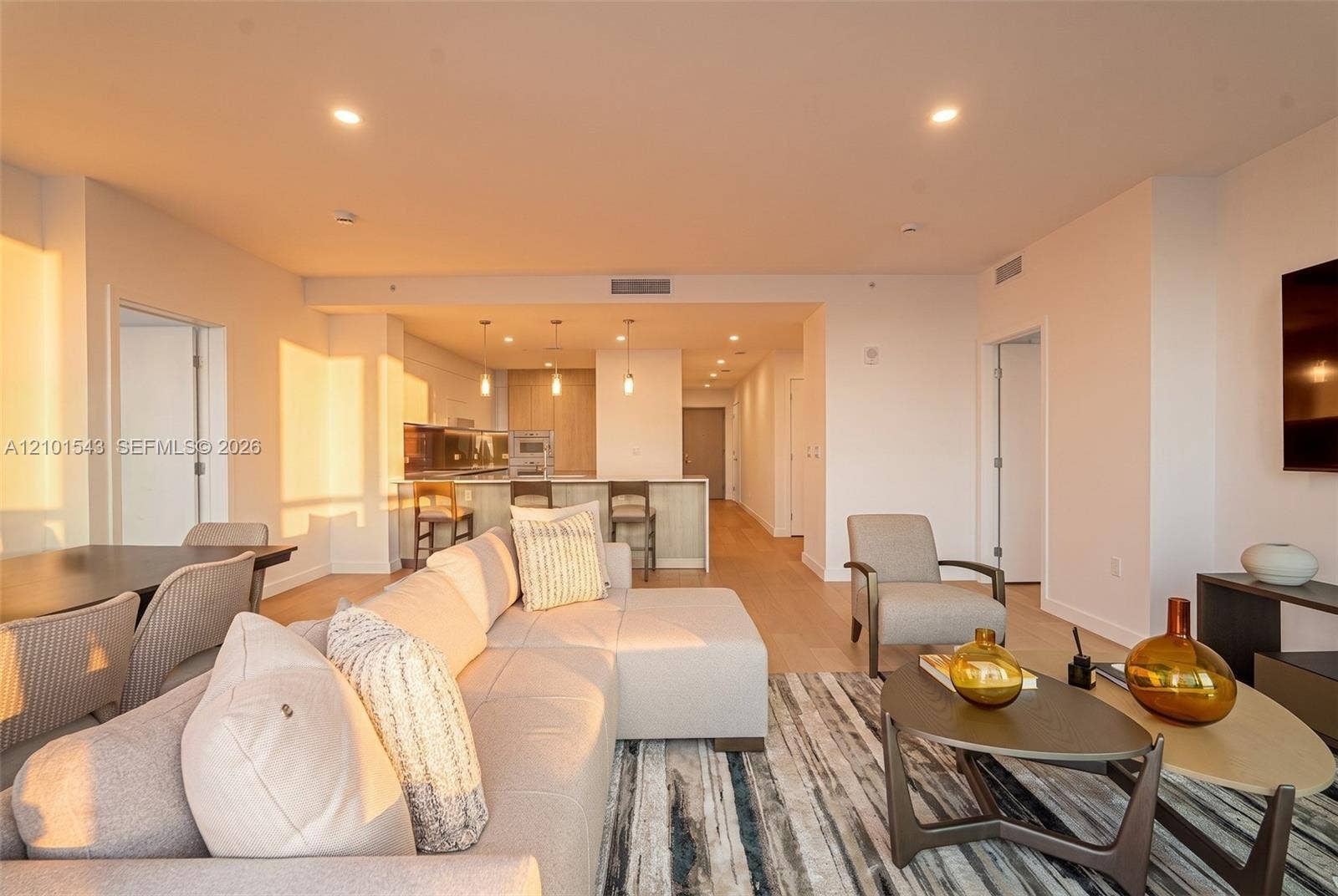 Open-concept living space featuring wood-finish flooring, recessed lighting, and a kitchen equipped with a stone-top island, built-in cabinetry, and multi-pendant lighting