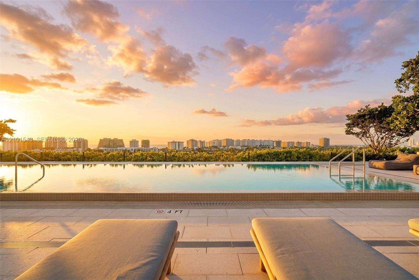 Infinity-edge swimming pool featuring stone tile decking, metal entry handrails, and a horizon backdrop