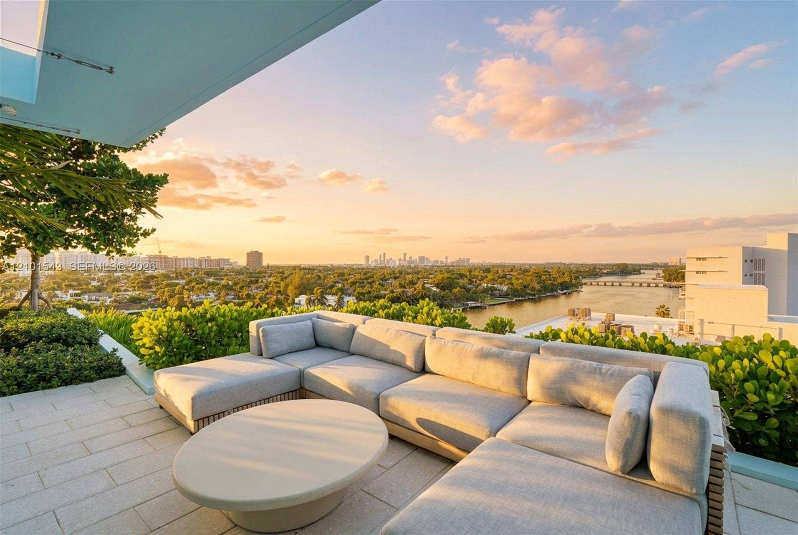 Expansive rooftop terrace featuring stone paver flooring, built-in planters with mature greenery, and a structural overhang