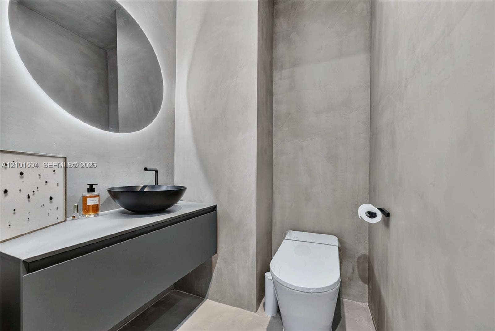 Powder room with floating vanity, vessel sink and round backlit mirror.