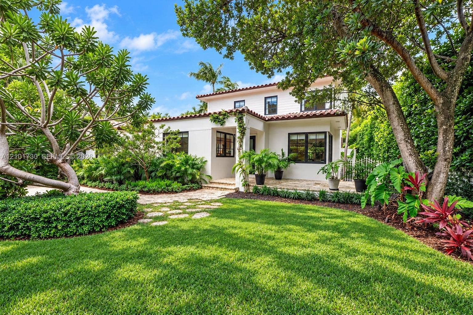 435 W 51st Street, Miami Beach, FL 33140 Two-story exterior featuring white stucco walls, dark-framed windows, and a terracotta tile roof, complemented by a stone paver patio and mature landscape