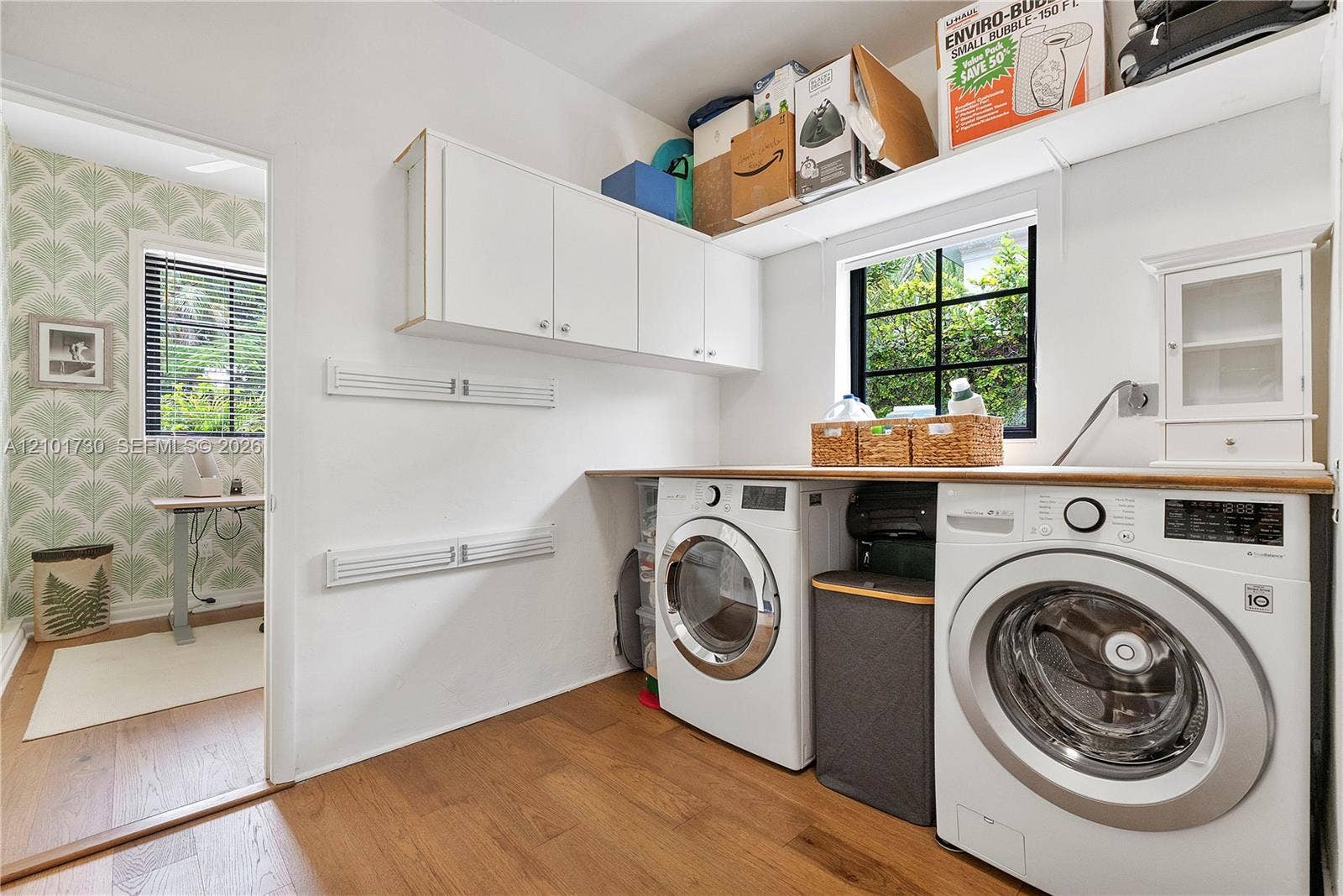 435 W 51st Street, Miami Beach, FL 33140 Laundry area featuring white wall-mounted cabinetry, wood-finish flooring, a wood-surface countertop, and a window with black grid mullions