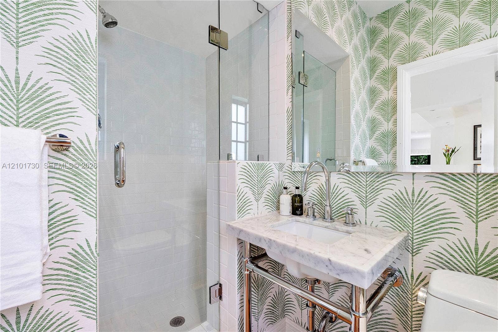 435 W 51st Street, Miami Beach, FL 33140 Wall-mounted washbasin with stone countertop, polished metal console legs, glass-enclosed shower featuring white subway tile, and wall-mounted faucet