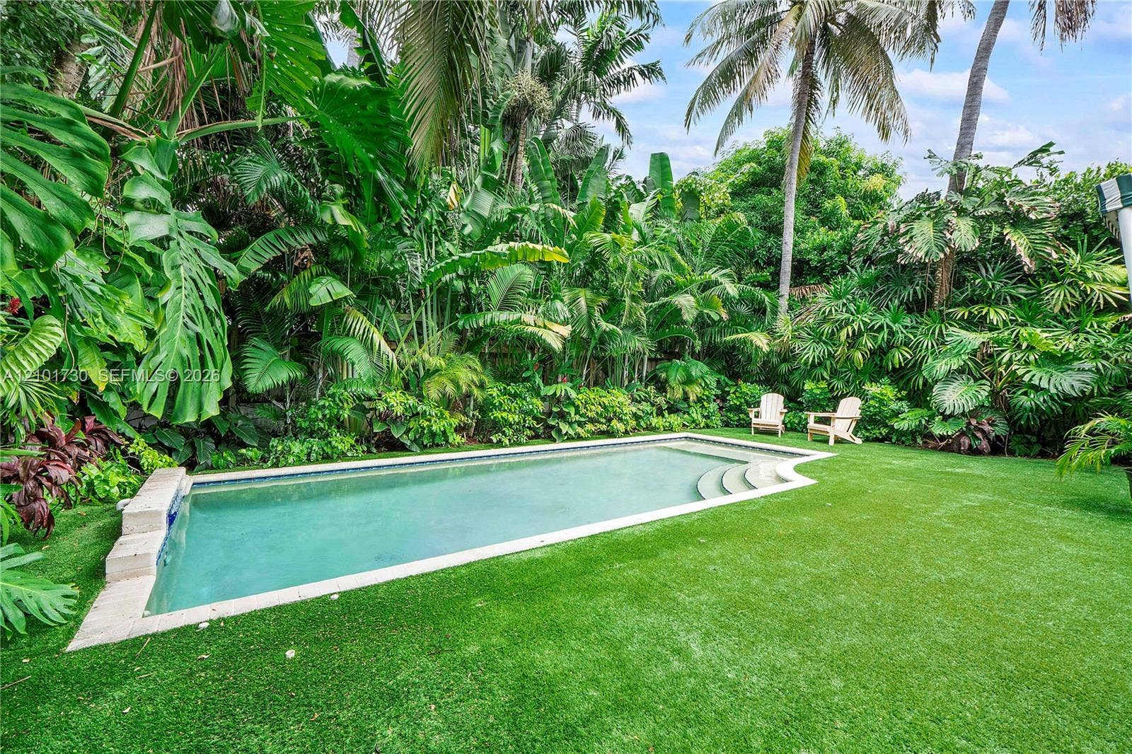 435 W 51st Street, Miami Beach, FL 33140 In-ground swimming pool featuring stone coping and built-in steps, surrounded by a lawn and dense tropical landscaping