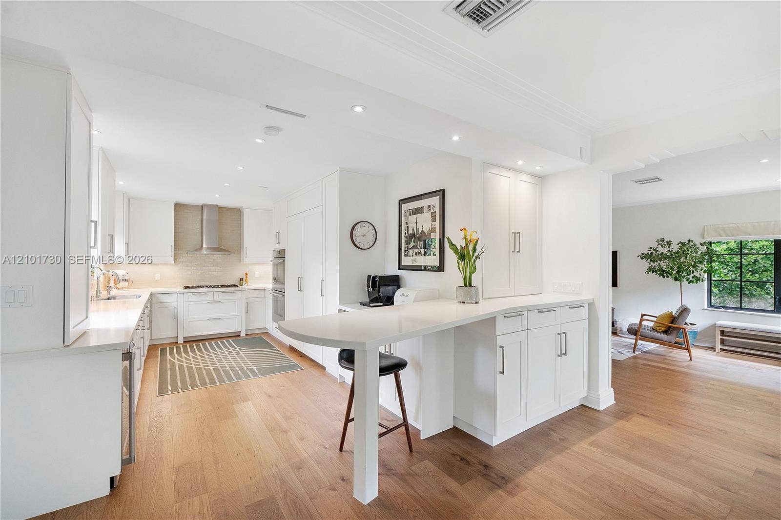435 W 51st Street, Miami Beach, FL 33140 Kitchen featuring white shaker-style cabinetry, quartz countertops, integrated peninsula, stainless steel range hood, and wood-finish flooring