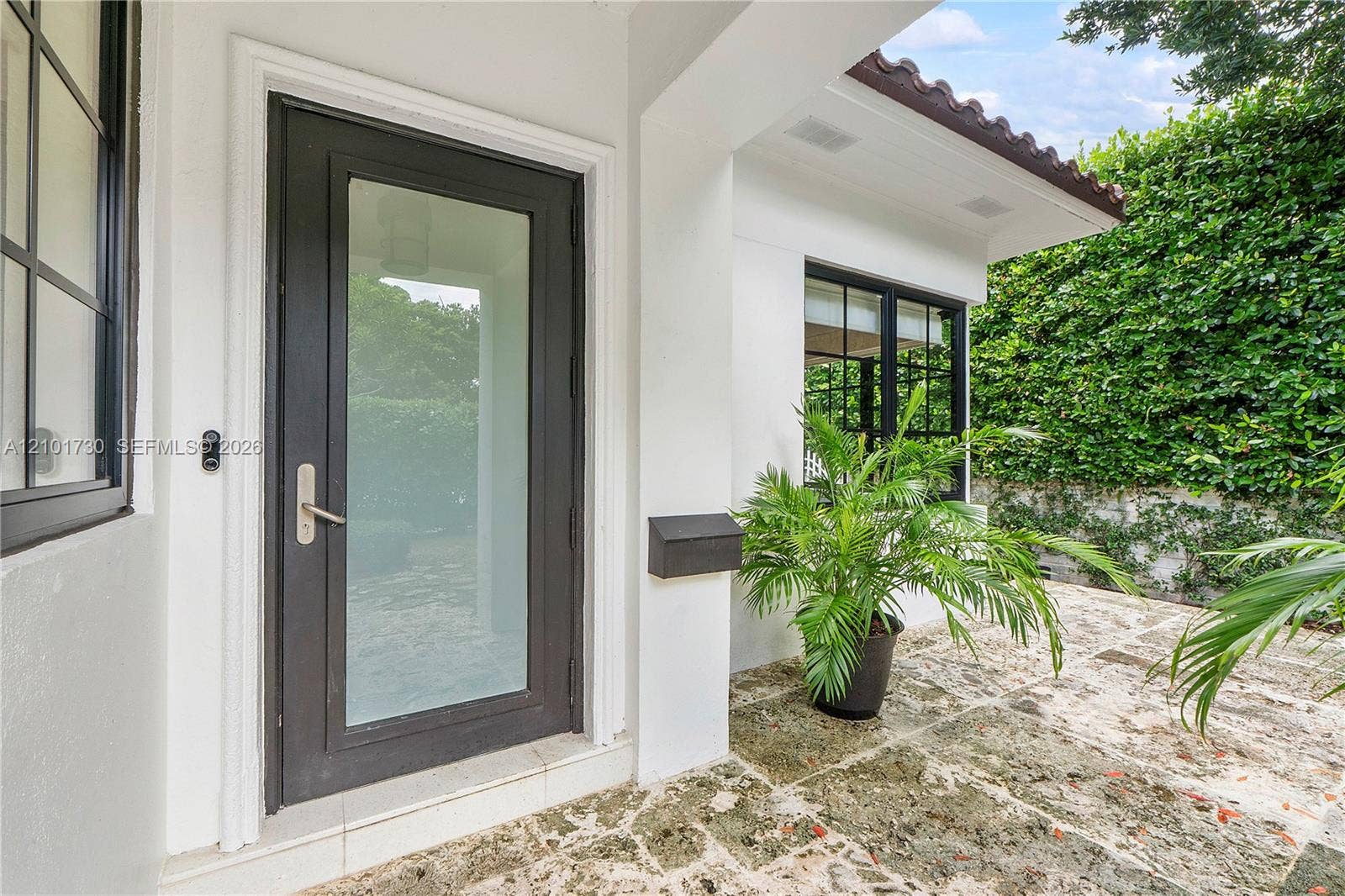 435 W 51st Street, Miami Beach, FL 33140 Entryway featuring a dark-framed glass door, natural stone paver flooring, a tile-accented roofline, and multi-pane windows with dark framing