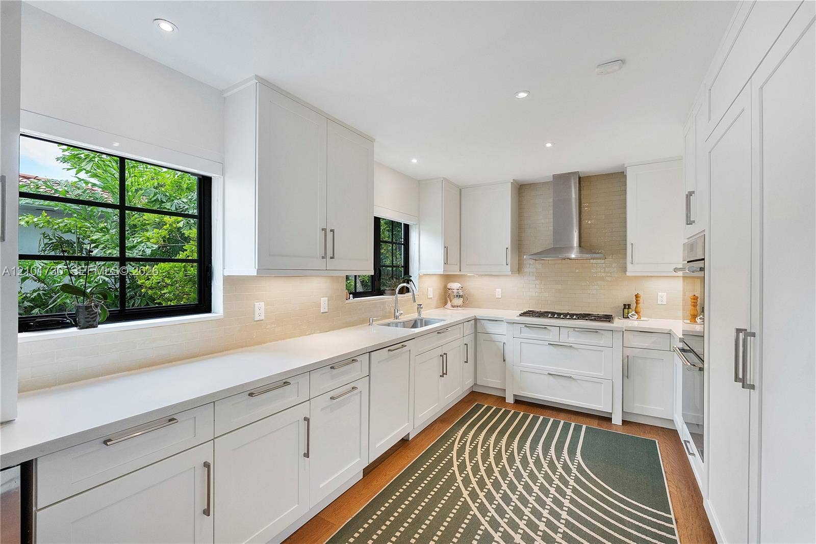 435 W 51st Street, Miami Beach, FL 33140 Kitchen featuring white shaker-style cabinetry, quartz countertops, subway tile backsplash, stainless steel ventilation hood, and wood-finish flooring