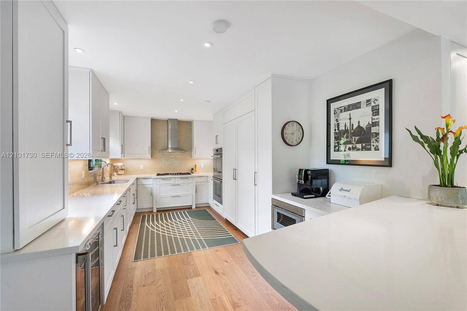 435 W 51st Street, Miami Beach, FL 33140 Kitchen featuring white cabinetry, solid-surface countertops, wood-finish flooring, built-in stainless steel appliances, and a tiled backsplash