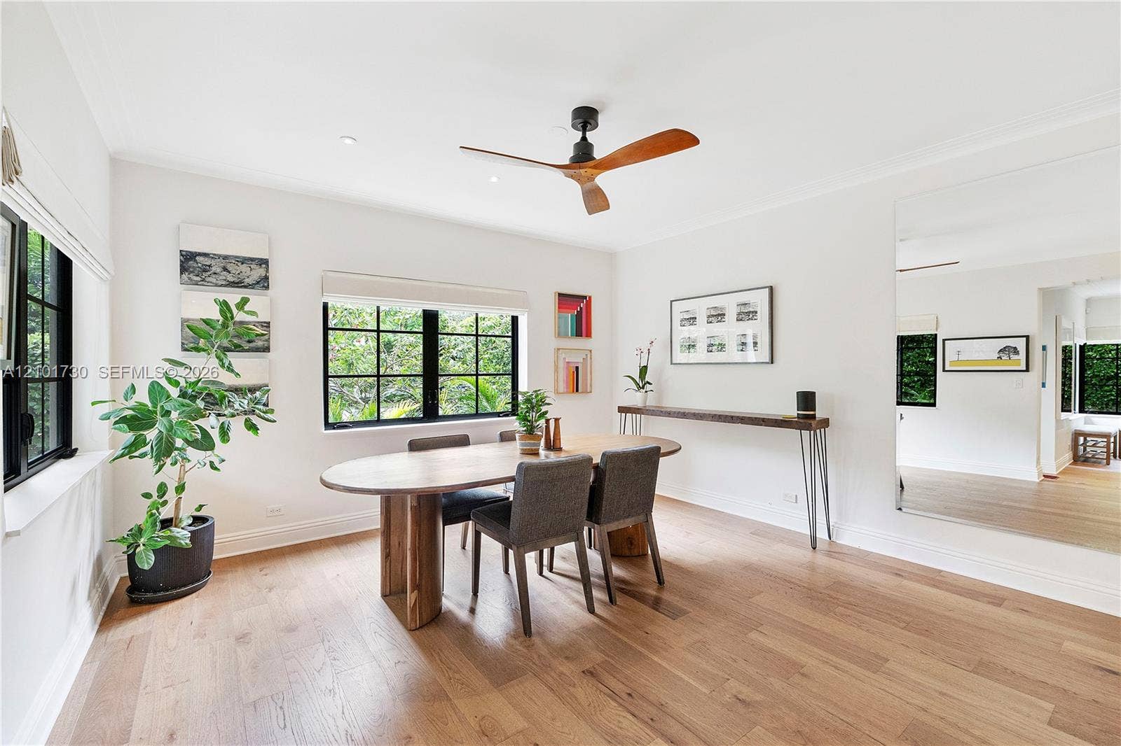 435 W 51st Street, Miami Beach, FL 33140 Spacious room featuring wood-finish flooring, black-framed windows, a ceiling fan with wood-tone blades, and a large wall-mounted mirror