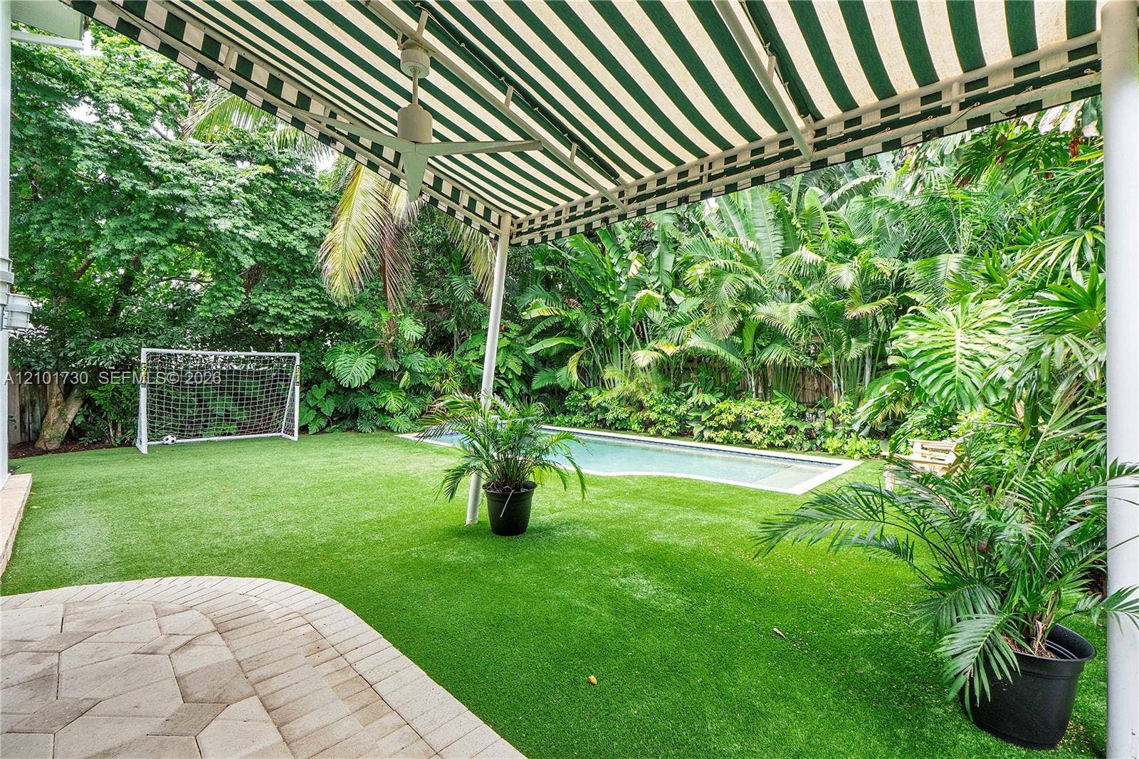 435 W 51st Street, Miami Beach, FL 33140 Backyard featuring a paver patio, a retractable striped awning, an in-ground pool, and synthetic turf