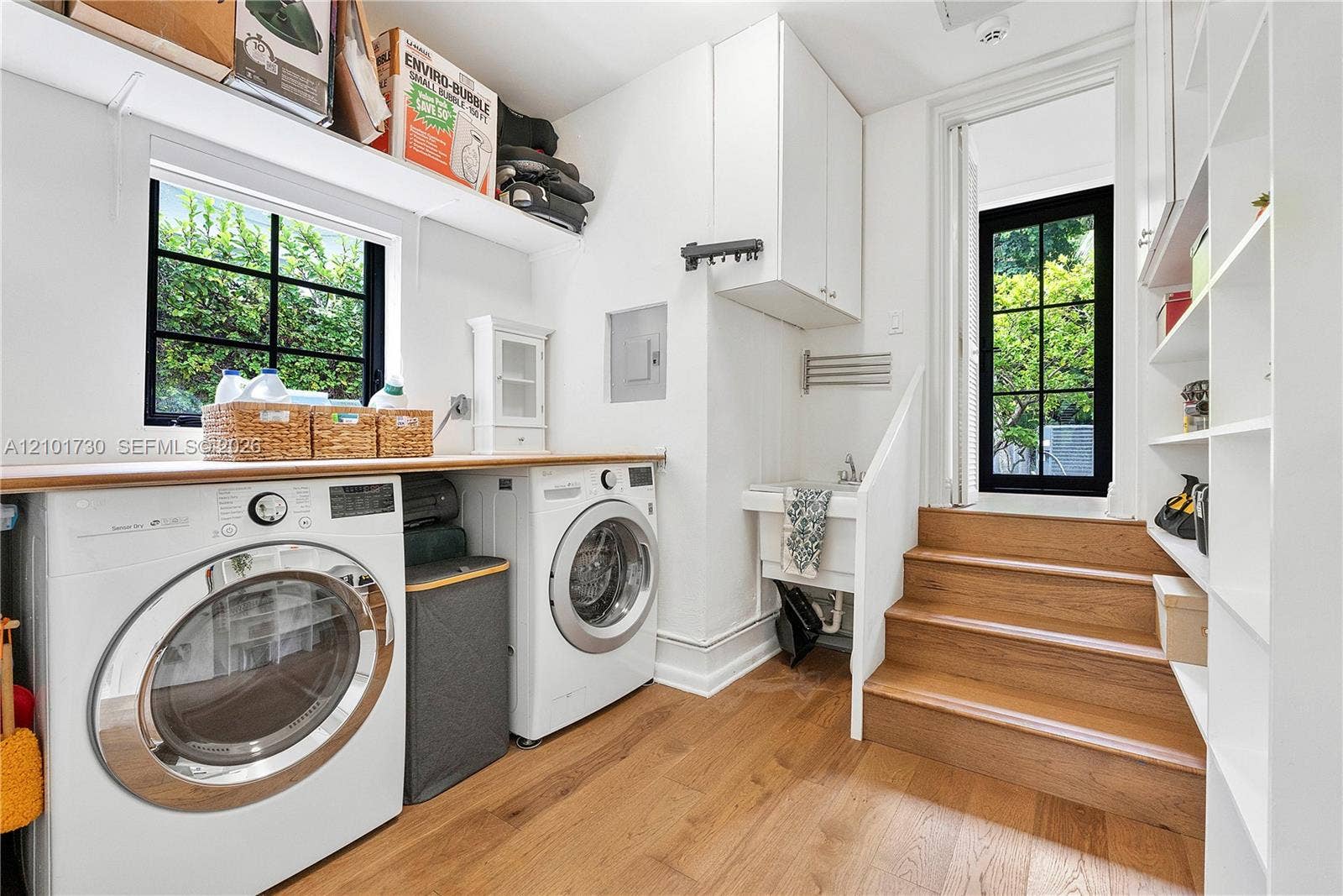 435 W 51st Street, Miami Beach, FL 33140 Laundry area featuring wood-finish flooring, built-in shelving, white cabinetry, a utility sink, and black-framed grid windows