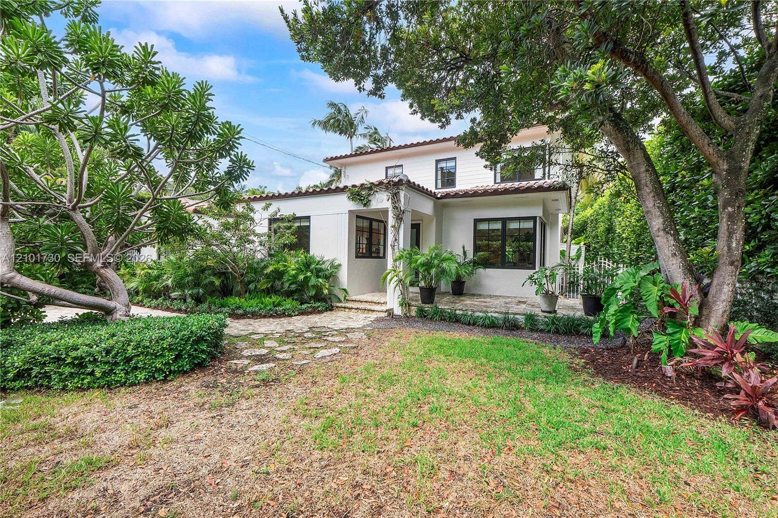 435 W 51st Street, Miami Beach, FL 33140 Two-story residence featuring a smooth stucco exterior, multi-pane windows, a tile roof, and a natural stone-paved patio surrounded by mature landscape