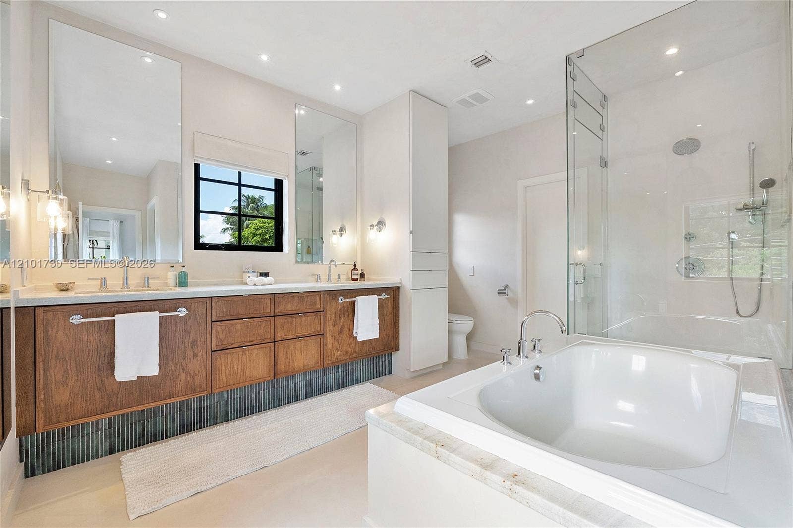 435 W 51st Street, Miami Beach, FL 33140 Bathroom featuring a dual-sink floating vanity with wood cabinetry, a glass-enclosed shower, a deep soaking tub with stone surround, and tall floor-to-ceiling built-in storage