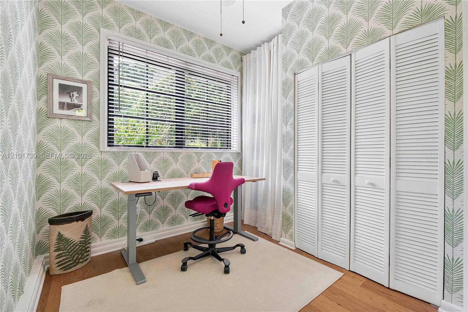 435 W 51st Street, Miami Beach, FL 33140 Room featuring palm leaf patterned wallpaper, wood-finish flooring, a multi-pane window with horizontal blinds, and a built-in closet with white louvered doors