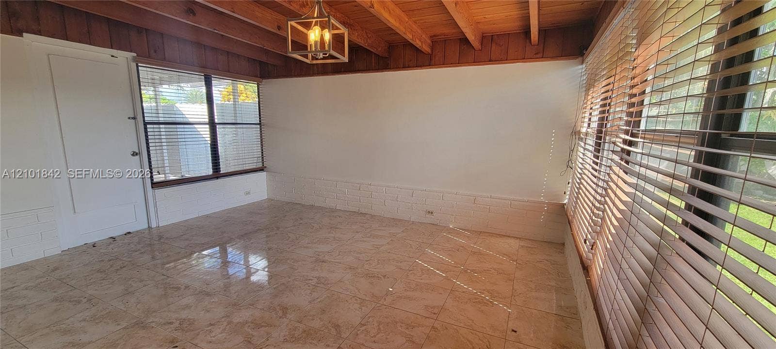 5795 W 13th Court, Hialeah, Hialeah, FL 33012 Sunroom featuring a vaulted wood-beam ceiling, large-format tile flooring, exposed painted brick wainscoting, and large windows with horizontal blinds