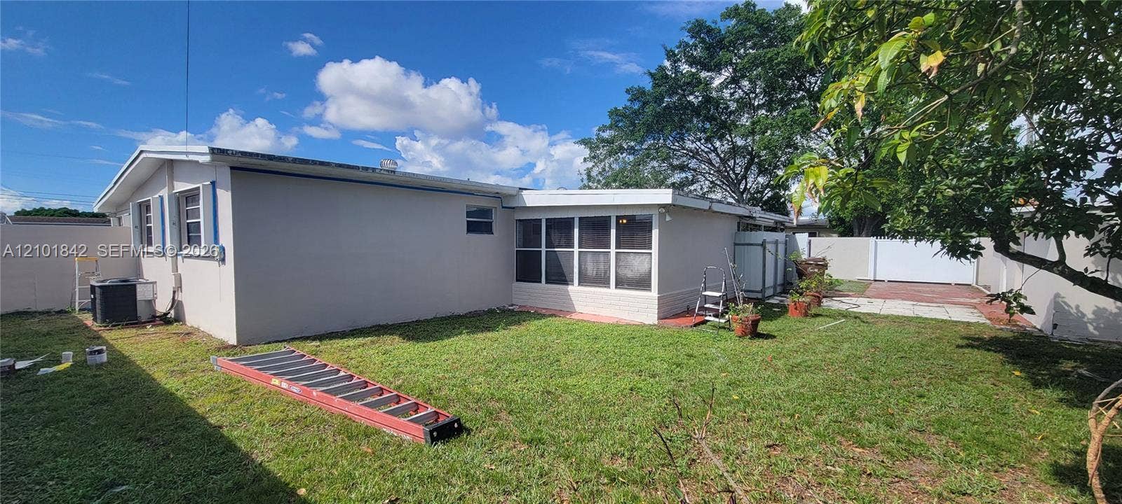 5795 W 13th Court, Hialeah, Hialeah, FL 33012 Exterior grounds featuring a grass lawn, enclosed sunroom with multi-pane windows, privacy fencing, and a concrete patio area