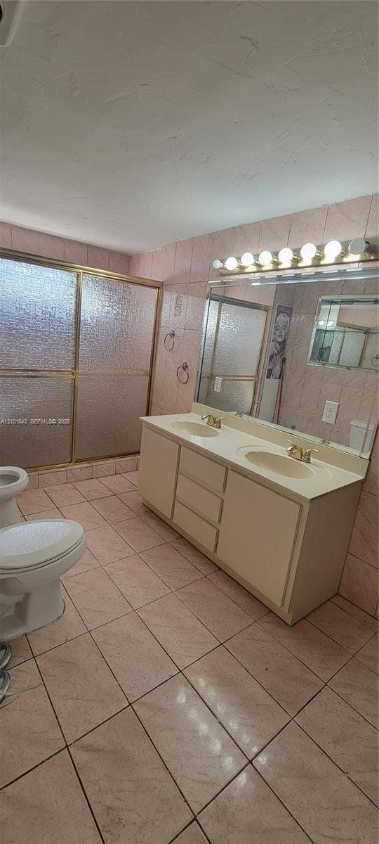 5795 W 13th Court, Hialeah, Hialeah, FL 33012 Double vanity with integrated sinks, large wall-mounted mirror, brass-finish fixtures, and walk-in shower with textured glass enclosure