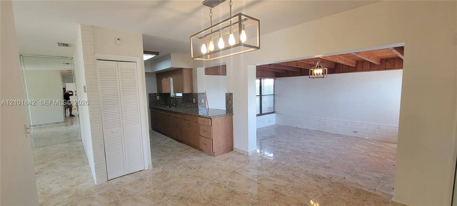 5795 W 13th Court, Hialeah, Hialeah, FL 33012 Open-concept interior featuring large-format tile flooring, a kitchen with stone countertops and wood cabinetry, exposed wooden ceiling beams, and a rectangular metal-frame pendant light fixture