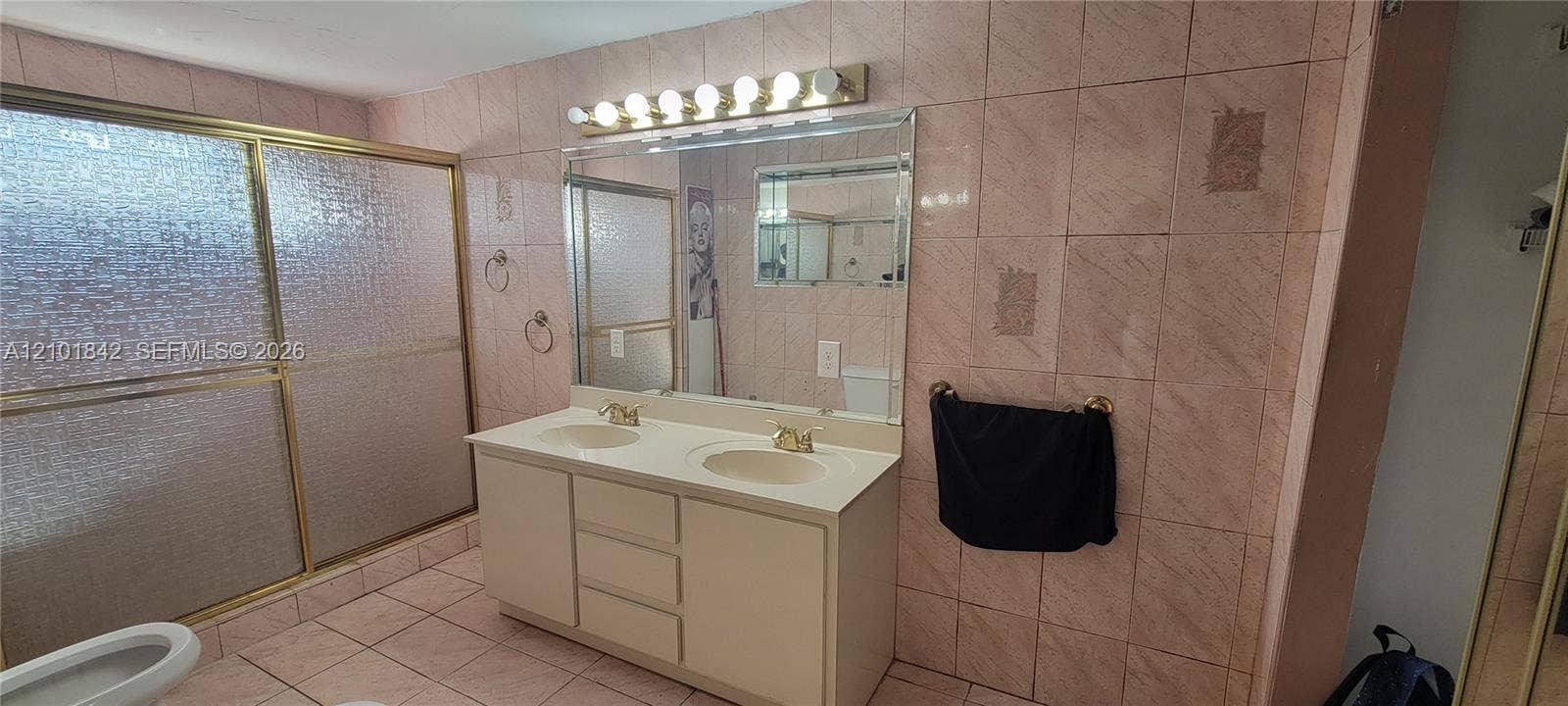 5795 W 13th Court, Hialeah, Hialeah, FL 33012 Dual-sink vanity with a solid-surface countertop, full-width vanity mirror, eight-bulb horizontal light fixture, and floor-to-ceiling ceramic tile wall detailing