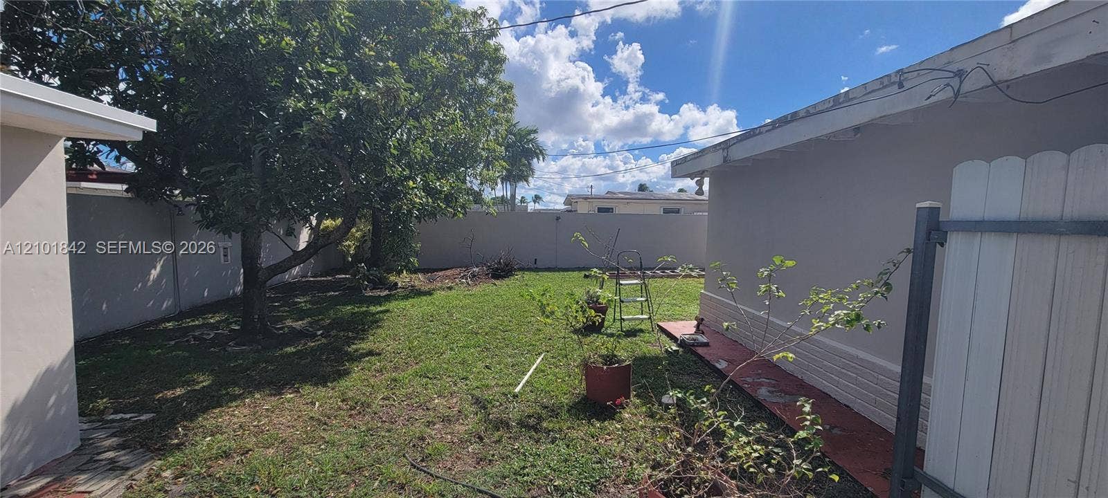 5795 W 13th Court, Hialeah, Hialeah, FL 33012 Enclosed backyard featuring a concrete perimeter wall, mature tree, grass lawn, and masonry exterior walls