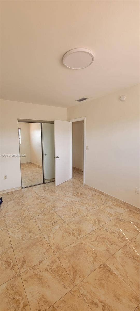 5795 W 13th Court, Hialeah, Hialeah, FL 33012 Room featuring polished stone-finish floor tiling, a sliding dual-panel mirrored closet, and a flush-mount circular ceiling fixture