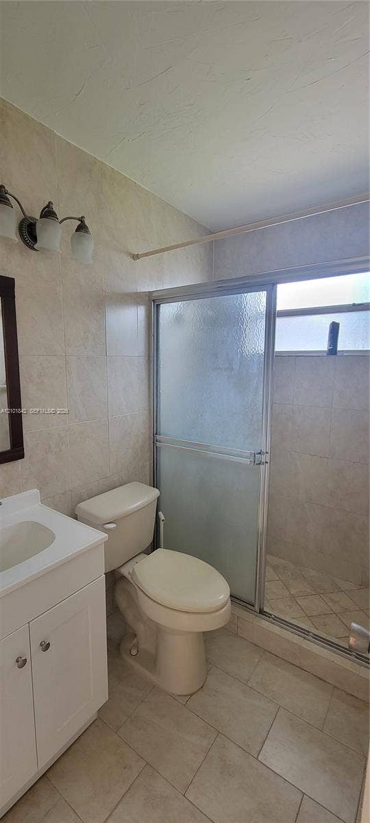 5795 W 13th Court, Hialeah, Hialeah, FL 33012 Bathroom featuring tile flooring, full-height wall tile surrounding the shower enclosure, a white vanity with an integrated sink, and a multi-light wall-mounted fixture