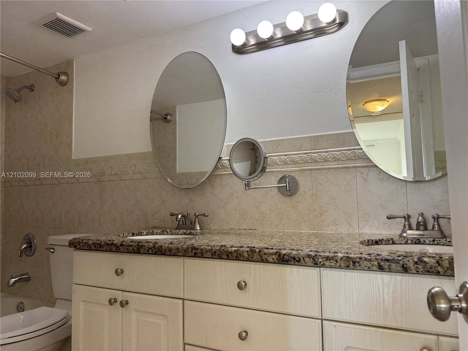 13120 SW 92nd Avenue, #B-PH1, Miami, Miami, FL 33176 Double vanity featuring a stone countertop with dual undermount sinks, light-finish cabinetry, two oval wall-mounted mirrors, and an adjustable magnifying vanity mirror