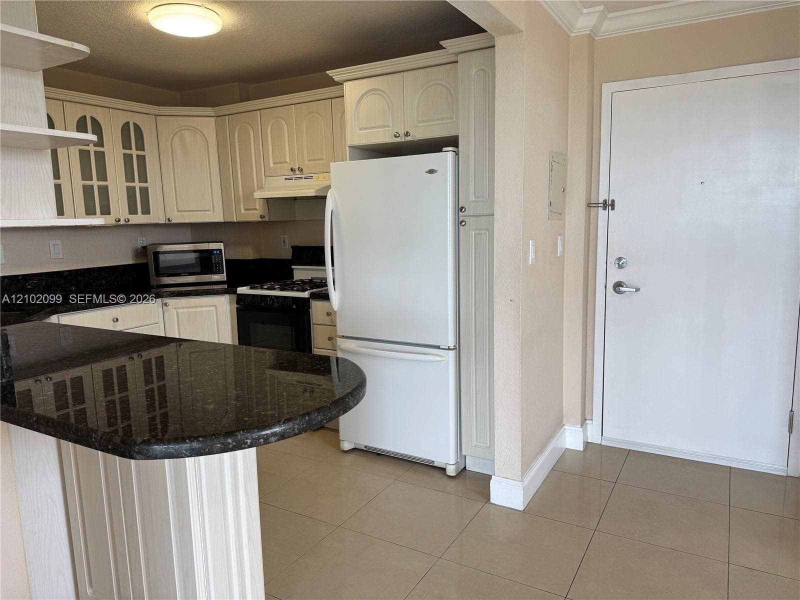 13120 SW 92nd Avenue, #B-PH1, Miami, Miami, FL 33176 Kitchen featuring a peninsula with dark stone countertops, off-white cabinetry with glass-panel upper doors, tile flooring, and integrated white appliances