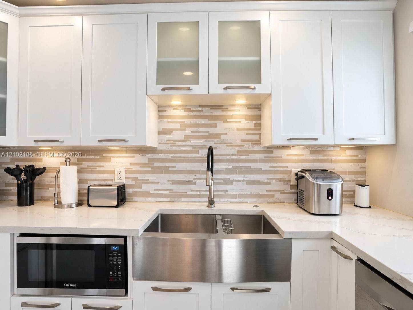 Kitchen featuring white shaker-style cabinetry with glass-front uppers, solid surface countertops, a horizontal mosaic tile backsplash, and an undermount stainless steel farmhouse sink with a high-arc pull-down faucet